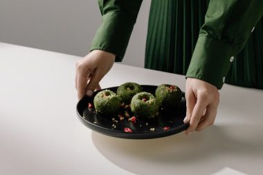 Hands presenting a black plate with spinach pkhali, showcasing traditional Georgian vegan cuisine.