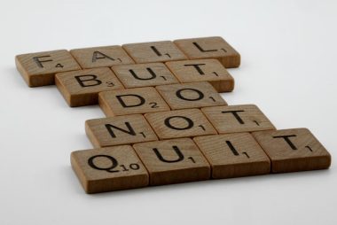 Wooden Scrabble tiles arranged to spell 'Fail but do not quit,' inspiring determination.